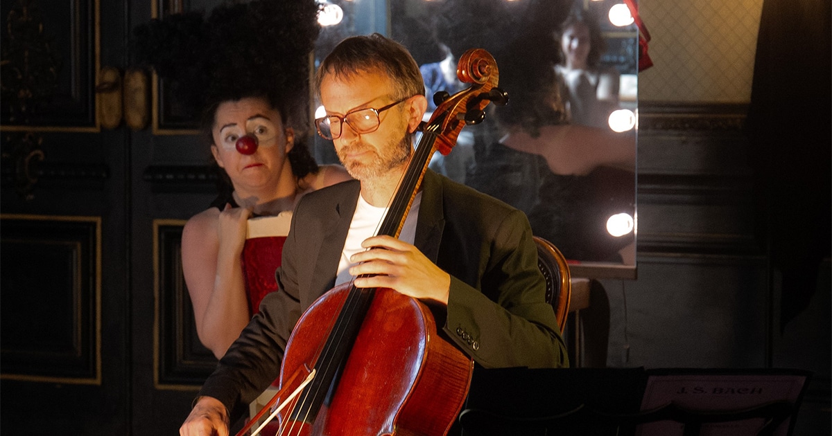 Sisi la clown derrière un violoncelliste, le fixant avec un regard inquiet.