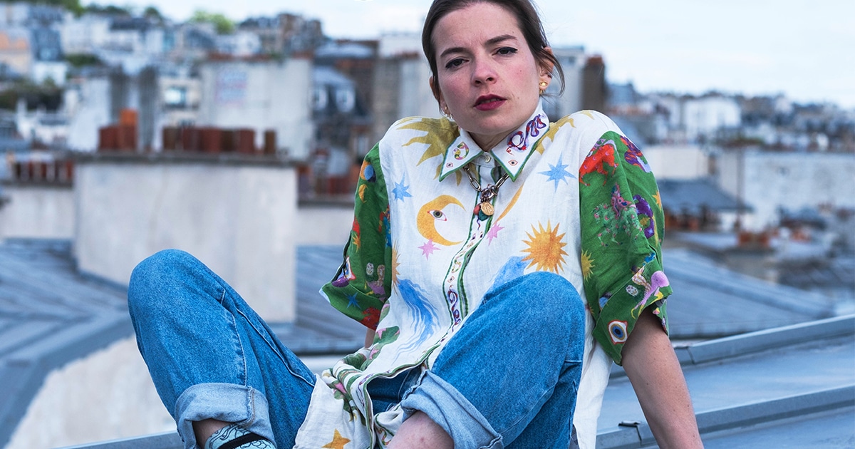 Manon Bril assise sur un toit, regardant l’objectif, en contre-plongée.