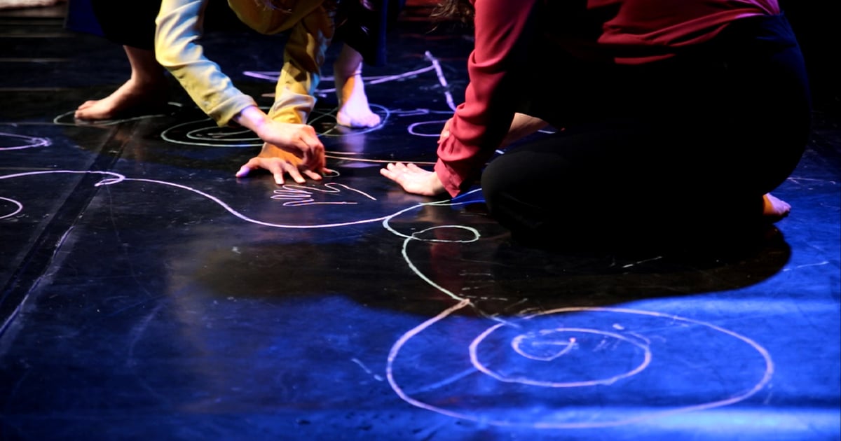 Personnes accroupies sur une scène décorée de motifs dessinés à la craie.