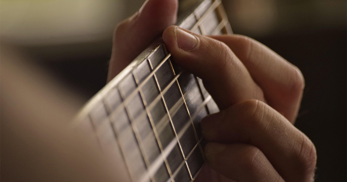 Main en train de jouer de la guitare acoustique, captée en gros plan.