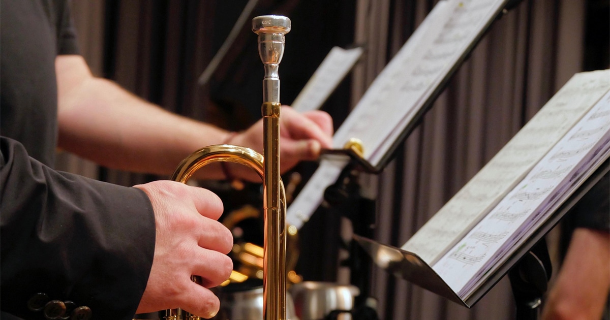 Main tenant un trombone, avec des partitions sur des pupitres à l’arrière-plan.