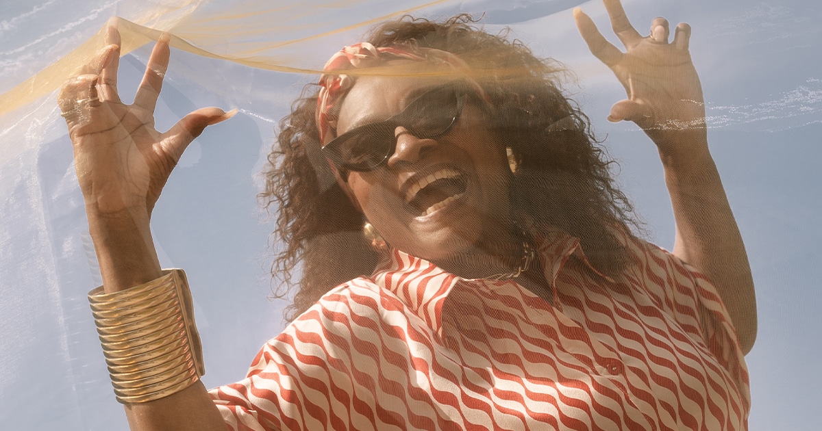 Linda Lee Hopkins, expressive, plaquée contre un voile transparent soufflé par le vent.