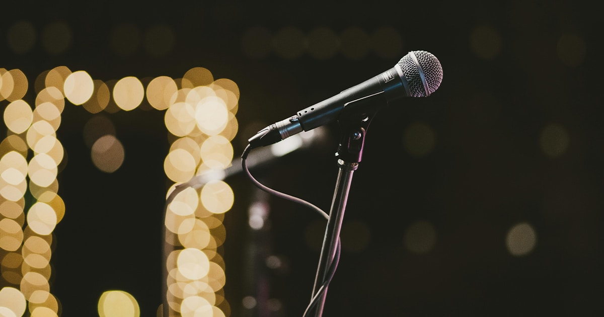 Gros plan sur un micro dans la pénombre, devant un mur de lumières jaunes.